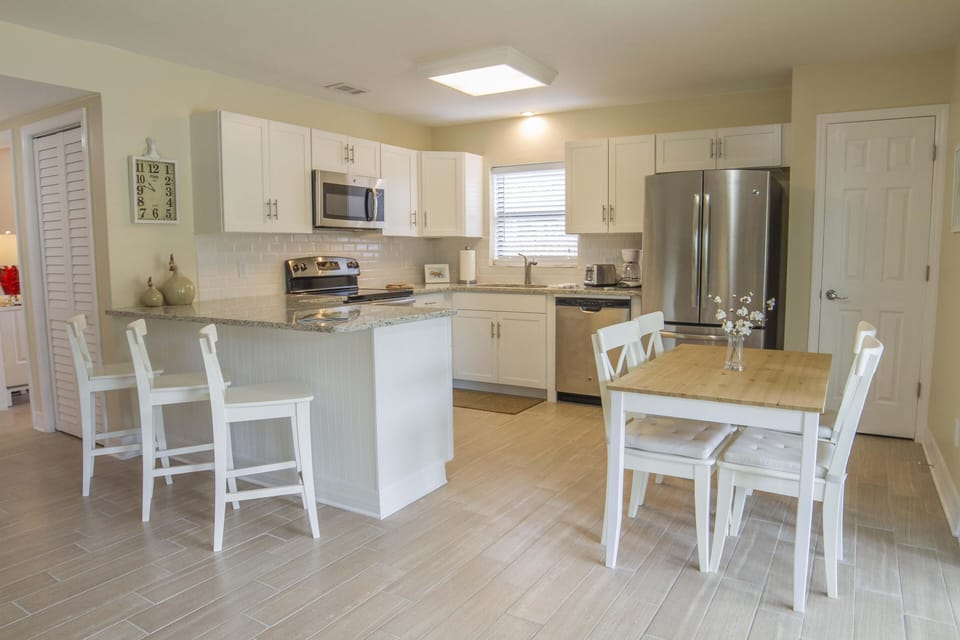 White cabinetry and granite countertops surround stainless steel appliances in the kitchen and dining area.