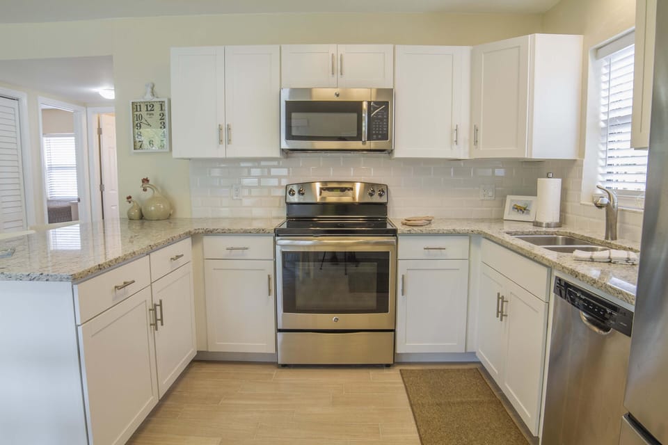 Stainless steel stove and microwave sit between white cabinets and granite countertops in the kitchen.