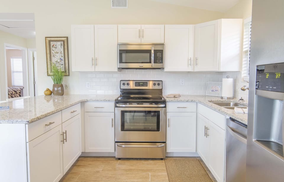 Stainless steel oven and microwave sit between white shaker cabinets and granite countertops in bright kitchen.