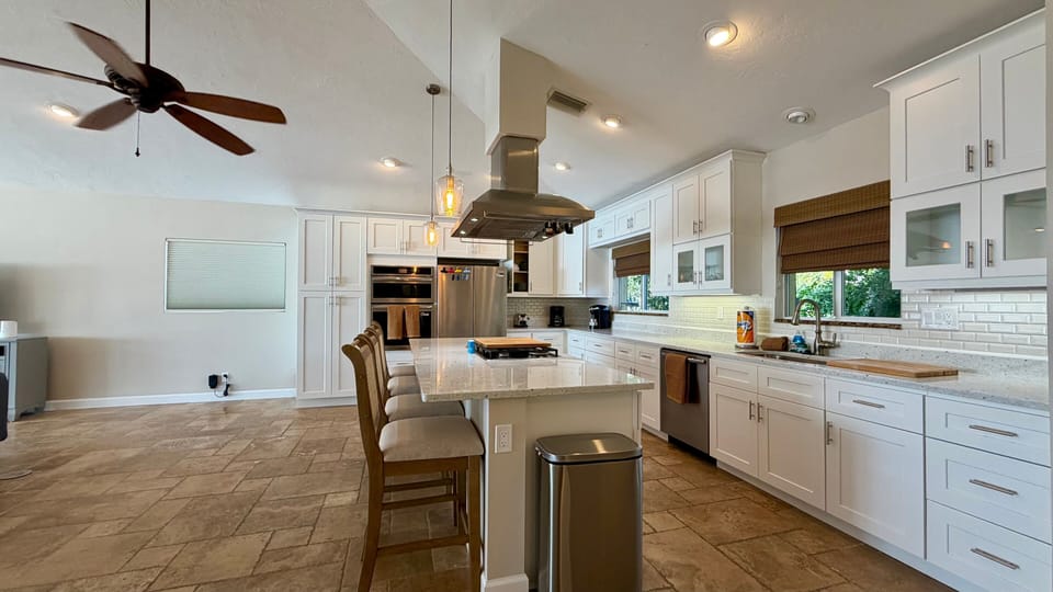 Gourmet kitchen with large center island, bar seating, stainless steel appliances, ceiling fan, and custom white cabinetry
