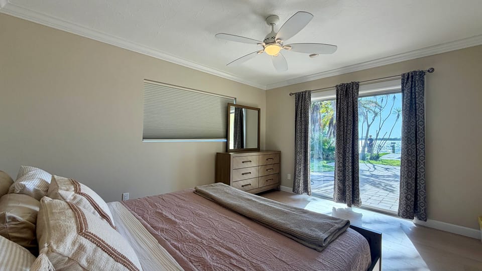 Master bedroom with king bed, waterfront views through large windows, and access to the outdoor living area