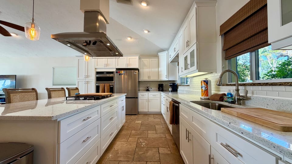 Kitchen featuring white shaker cabinets, stone countertops, stainless steel refrigerator, and generous prep space along the island