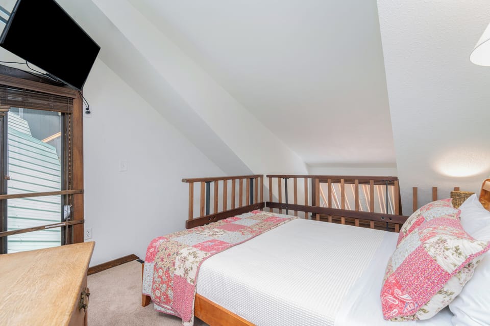 Your cozy loft bedroom features a charming wooden railing, plush bedding with warm quilted accents, and modern entertainment for peaceful rest.