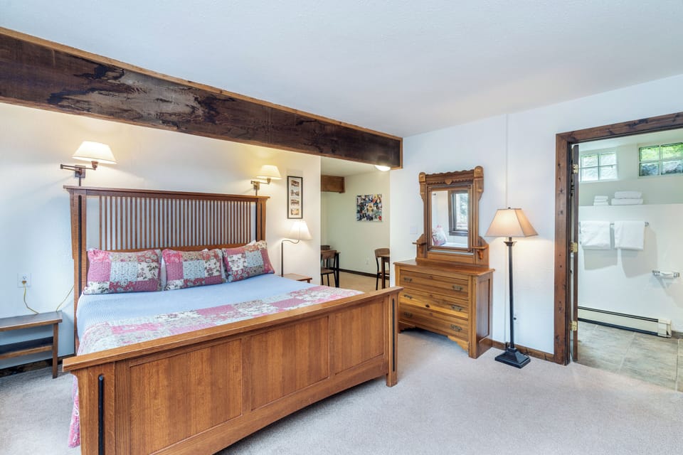 Unwind in this charming bedroom featuring rustic wooden beams, a cozy handcrafted bed, and warm lighting that creates a peaceful retreat after your day exploring.