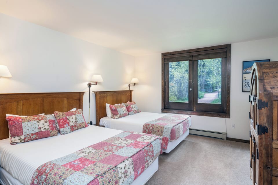 Sleep soundly in your cozy retreat with two plush beds dressed in charming quilts, warm lighting, and a peaceful view of the surrounding greenery through your private window.