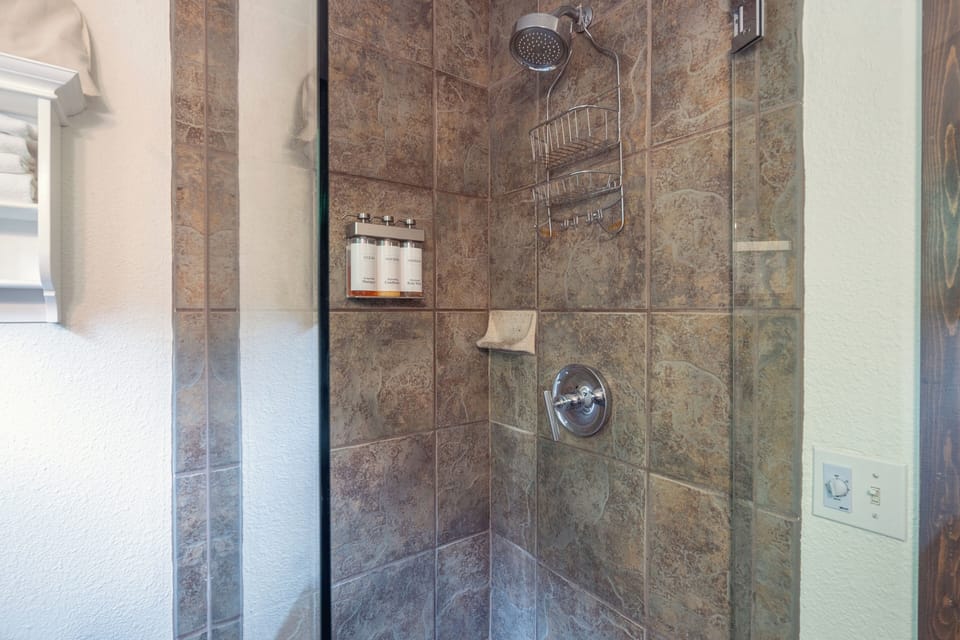 Step into your private shower with rainfall showerhead, natural stone tile, and premium amenities stocked for your comfort.