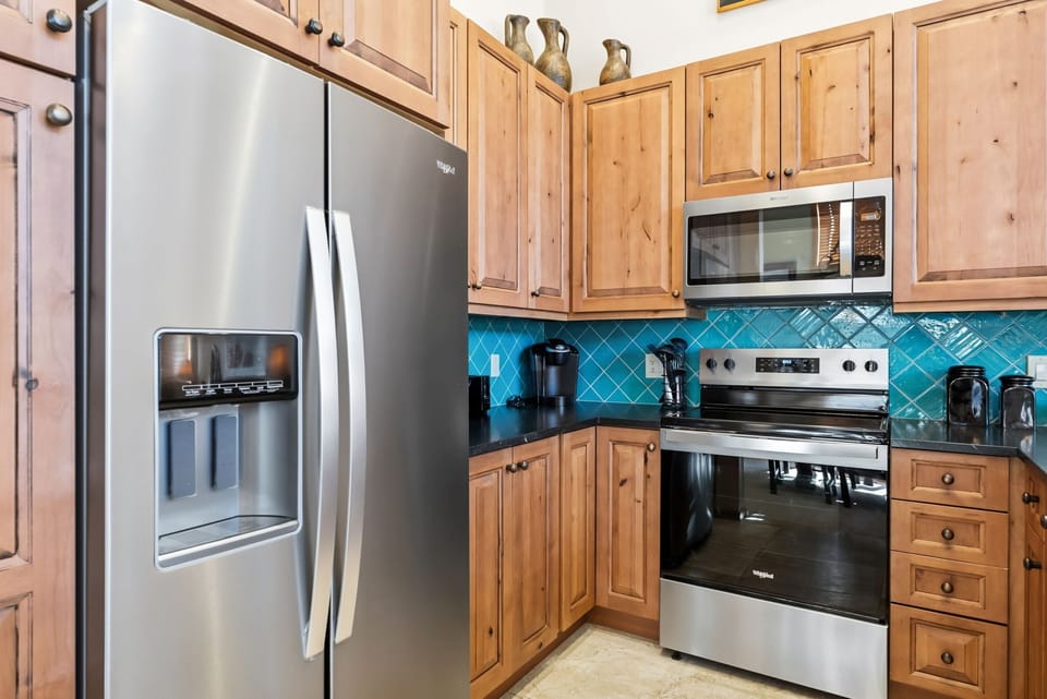 Cook your favorite meals in this fully equipped kitchen with stainless steel appliances, warm wood cabinetry, and stunning turquoise backsplash.