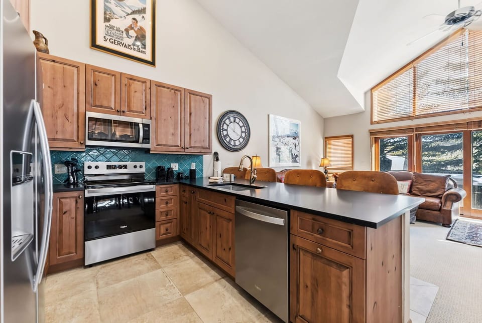 Your fully equipped kitchen features warm wood cabinetry and modern appliances, perfect for preparing meals with mountain views streaming through large windows.