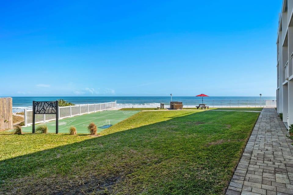 Patio shuffleboard court with green playing surface, lawn area, and paved walkway.