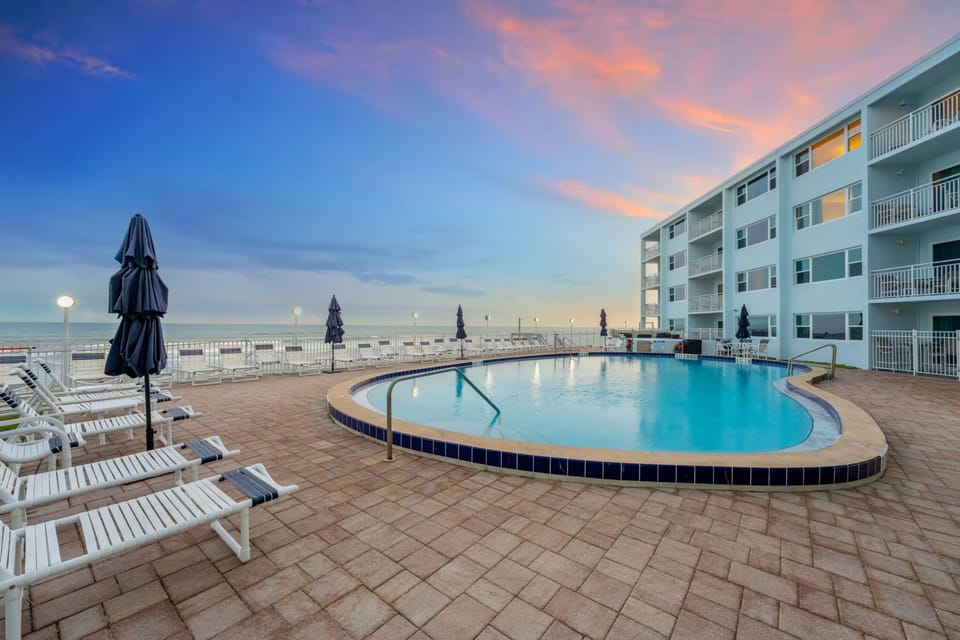 Oceanfront swimming pool with lounge chairs and umbrellas overlooking the beach at sunset