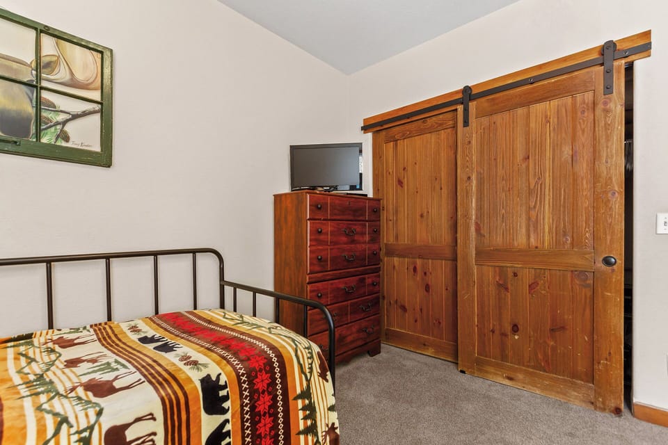 Cozy bedroom with rustic barn door, wood dresser, TV, and charming details. Your restful mountain retreat awaits with unique character and comfort.