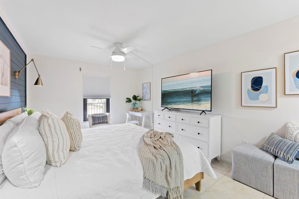 Spacious master bedroom with a king bed, stylish decor, and a large TV.