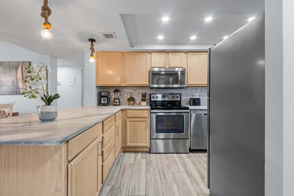 Modern kitchen with stainless steel appliances and stylish lighting.