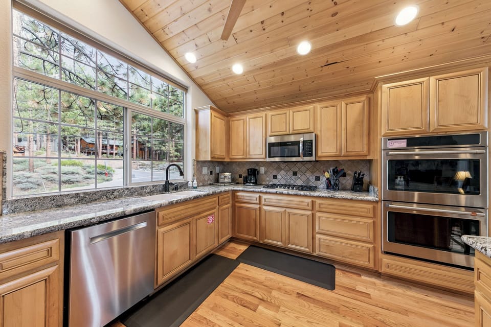 Your gourmet kitchen awaits with granite counters, stainless steel appliances, and warm wood finishes beneath soaring ceilings.