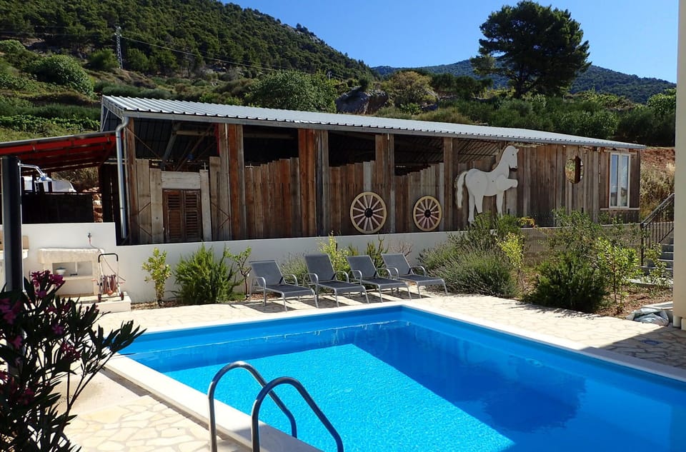 Pool and loungers with backdrop of olive groves and hills.