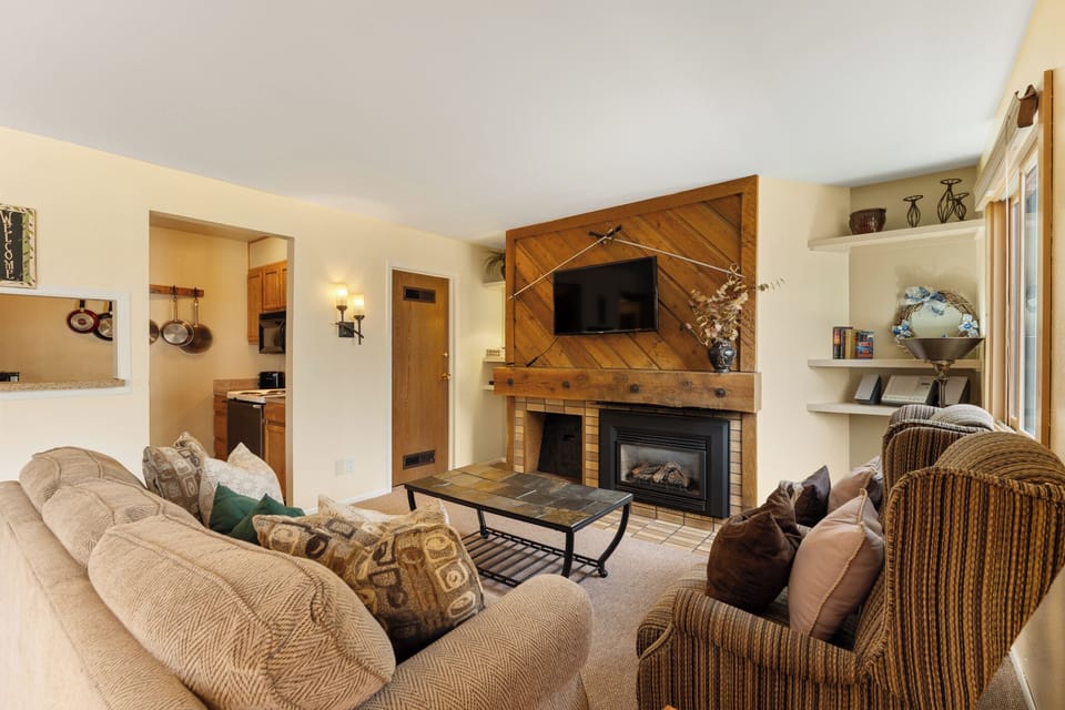Relax in your cozy living room, where plush sofas surround a warm fireplace beneath a stunning wood accent wall. Open shelving displays curated touches, while soft lighting invites peaceful evenings.