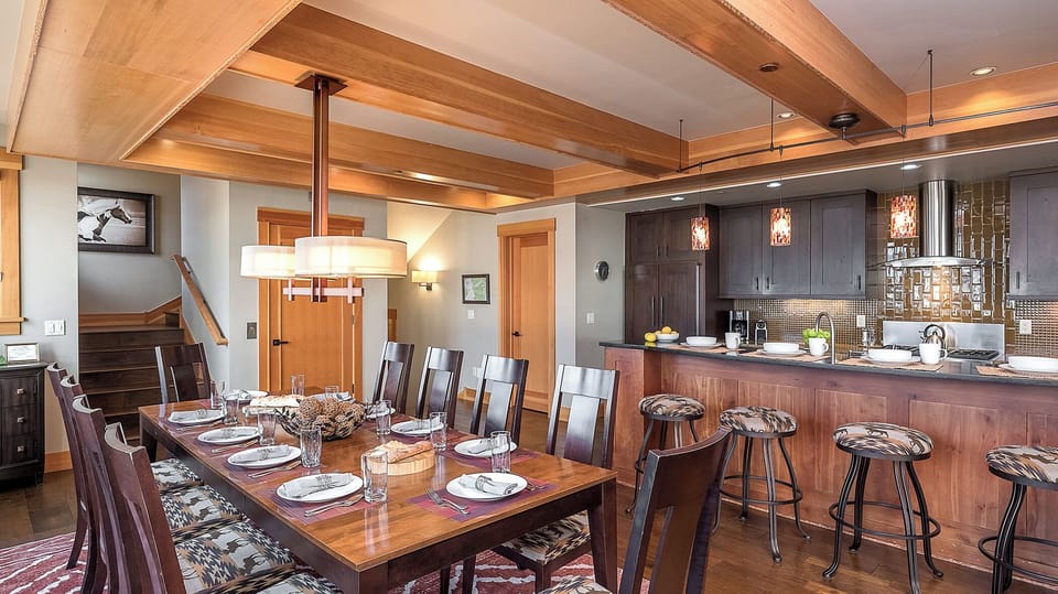 Gather around the stunning wood dining table or pull up a stool at the kitchen bar in this beautifully designed open-concept space, where warm beams and modern touches create an inviting atmosphere for your mountain retreat.