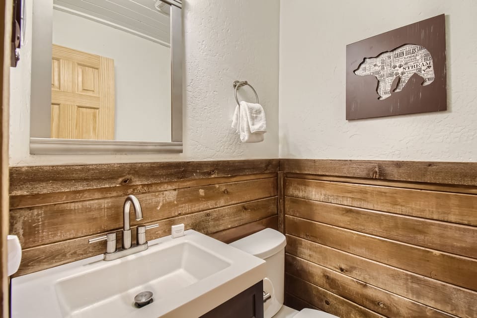 A small bathroom with a white sink, wooden walls, a mirror, a towel hanging, and a picture of a bear on the wall.