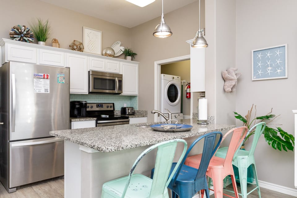 Your bright kitchen features granite counters, stainless appliances, and colorful coastal stools perfect for morning coffee or meal prep.