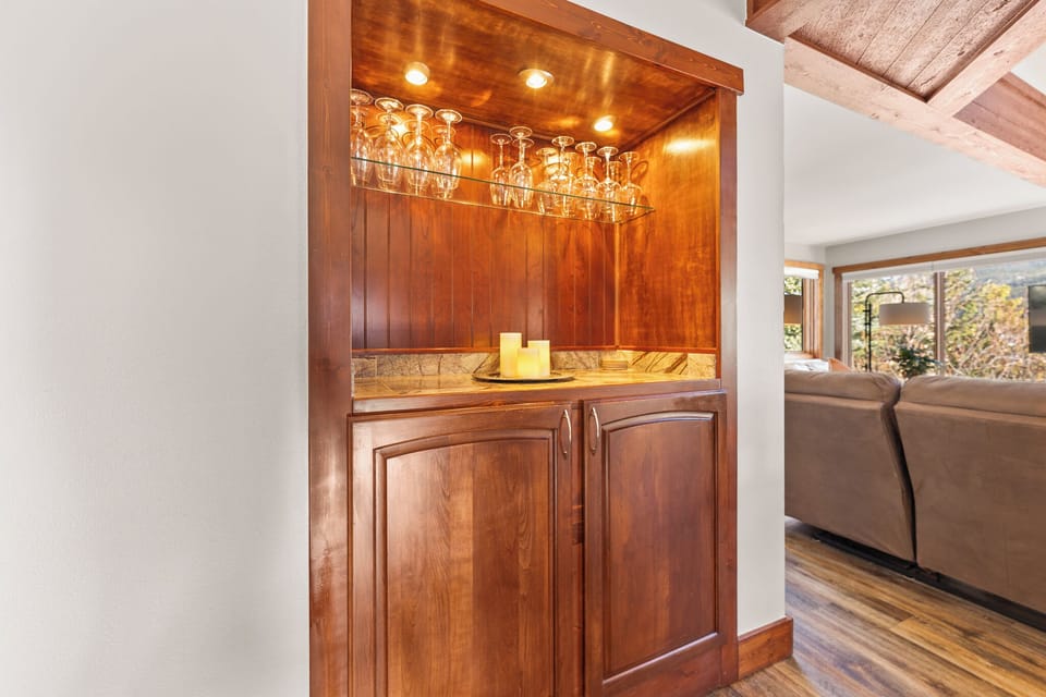 Your elegant wet bar awaits, featuring rich wood cabinetry and hanging glassware for effortless entertaining in style.