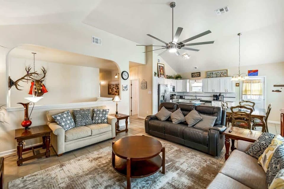 Open-concept living room with leather recliner, cream sofas, vaulted ceiling & large TV