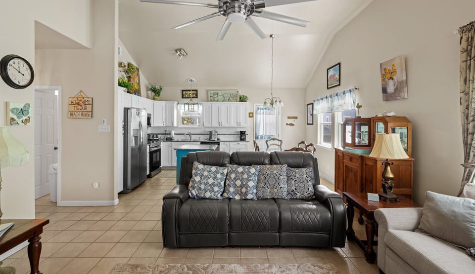 Open floor plan with leather sofa, kitchen island & 'Welcome to Our Beach House' sign