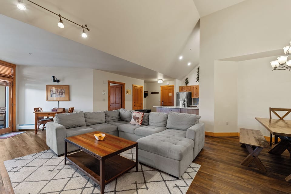 Relax in your spacious open-plan living area featuring plush gray sectional seating, warm wood accents, and soaring ceilings.