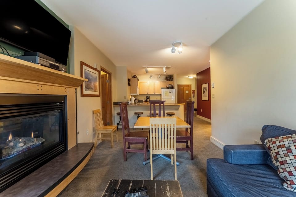 Cozy up by your crackling fireplace while enjoying meals at the wooden dining table, with a fully equipped kitchen just steps away.