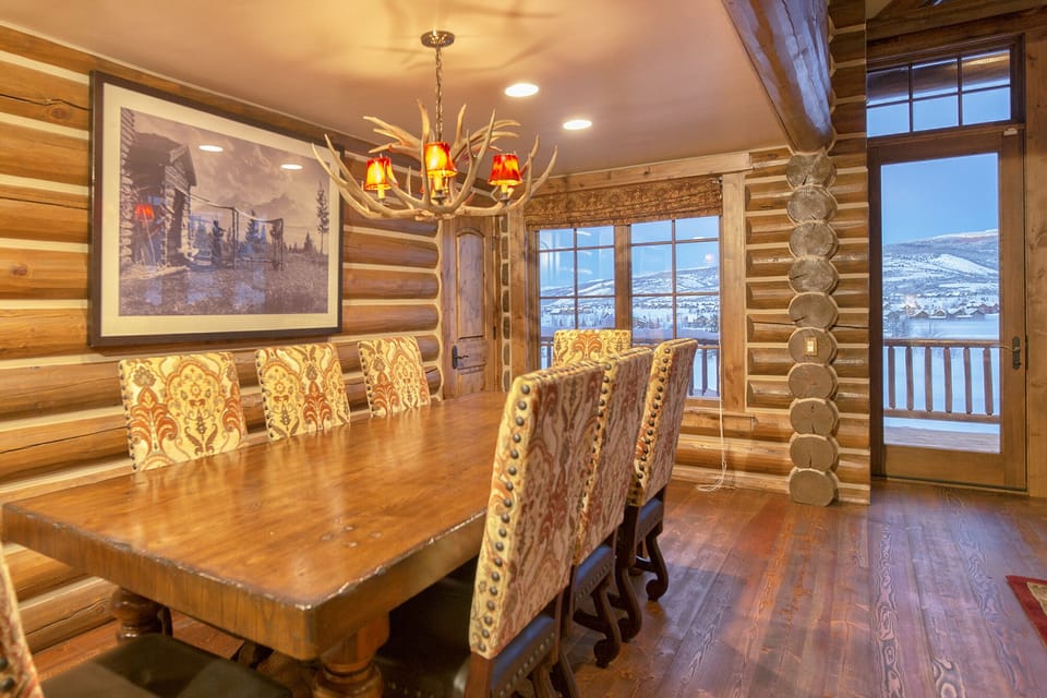 Gather around this stunning rustic dining room where warm log walls and an antler chandelier create the perfect mountain retreat atmosphere. You'll love sharing meals here while gazing at breathtaking snowy vistas through large windows.