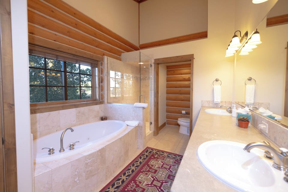 Unwind in your private spa-like retreat with a luxurious soaking tub positioned perfectly beneath the window for natural light as you bathe. The warm wood beams and elegant marble create a serene atmosphere.