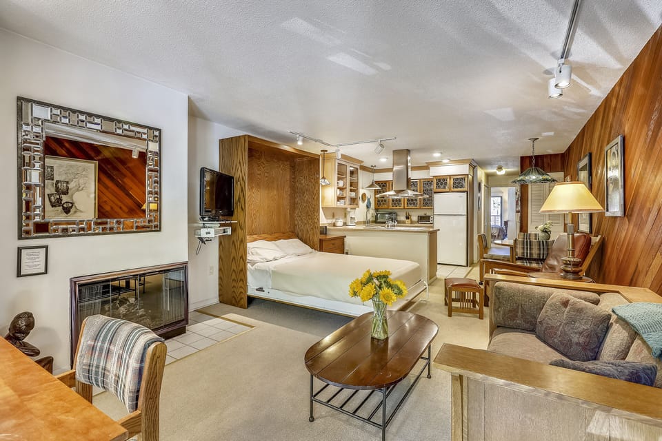 View from front entry over living room, queen Murphy bed, kitchen, eating area and hallway leading you to the bedroom with private deck.