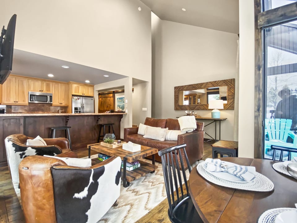 Bright open-concept living area with leather seating, rustic décor, vaulted ceilings, and seamless flow to the kitchen—perfect for relaxing après-ski.