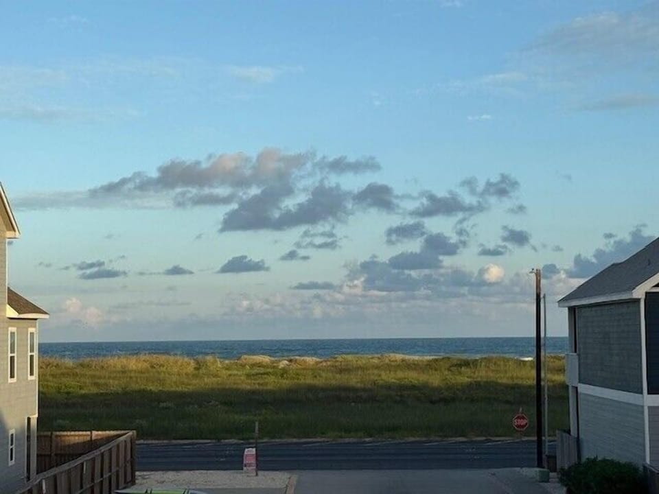 Ocean views stretch beyond coastal dunes and grasses, with neighboring beach houses framing this peaceful seaside setting.