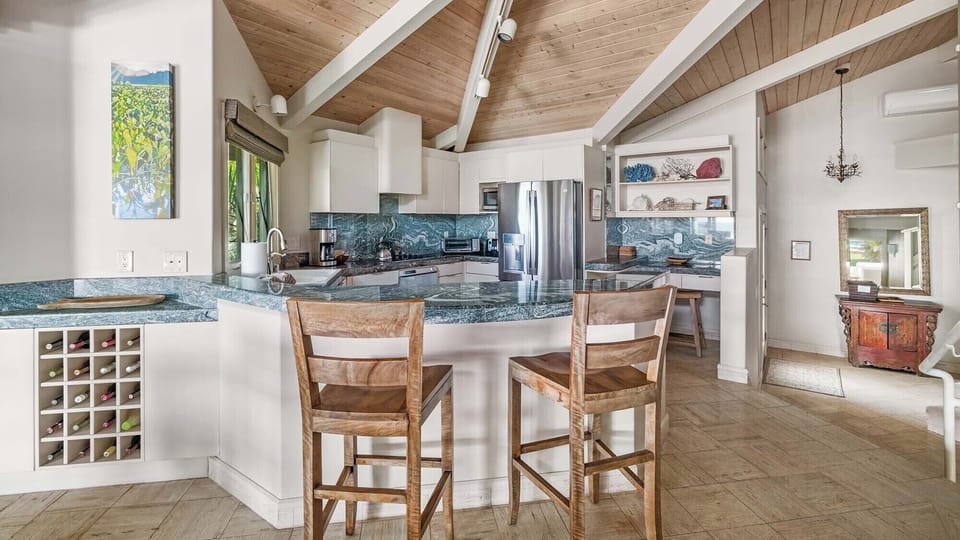 Step into your spacious gourmet kitchen with vaulted wood ceilings, gleaming granite counters, and modern stainless appliances—perfect for preparing meals while enjoying views of tropical greenery through the windows.