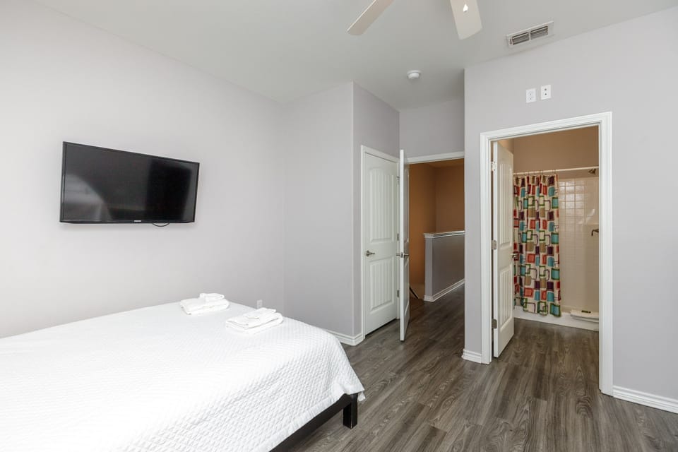 Your contemporary bedroom features crisp linens, a wall-mounted TV for entertainment, and your own private bathroom with colorful shower tile accents.