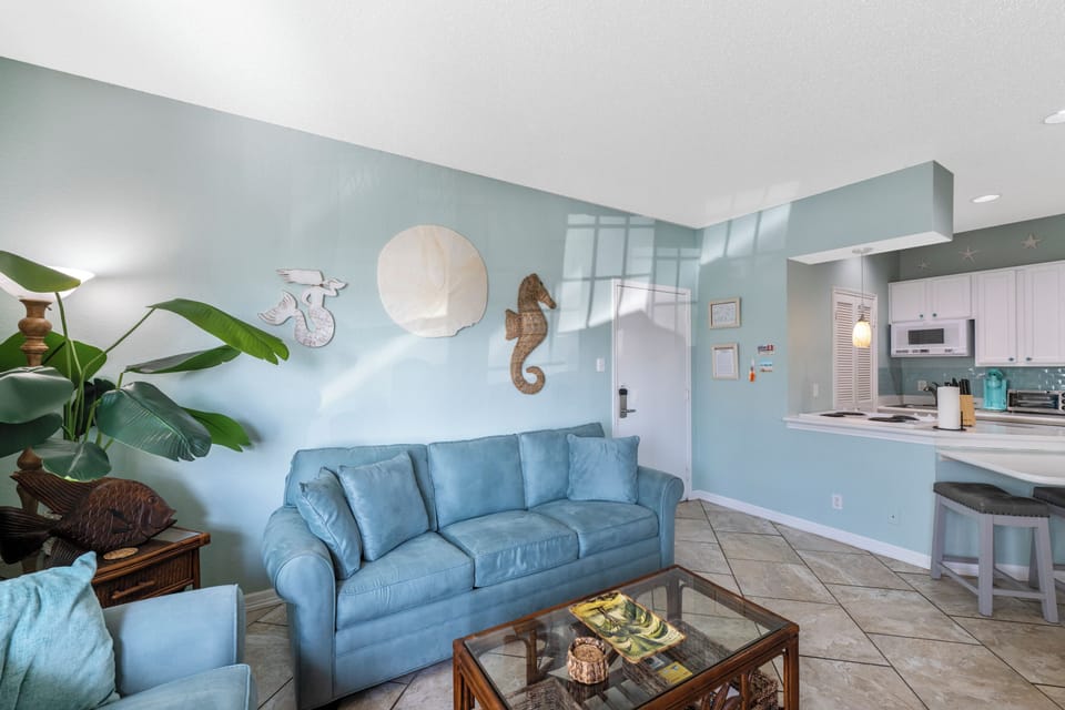 Relax in your coastal-themed living space with ocean-blue sofa, nautical decor, and open kitchen perfect for vacation cooking.