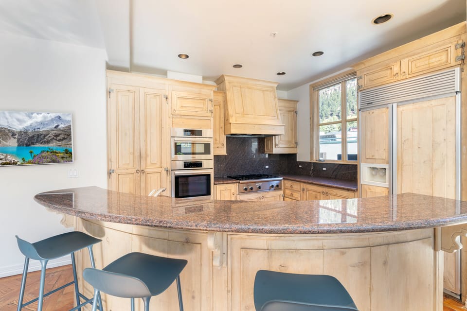 Open well equipped kitchen with Viking, Bosch and Thermodore appliances. Large counter with bar stools and wall mounted TV facing the living area seating.