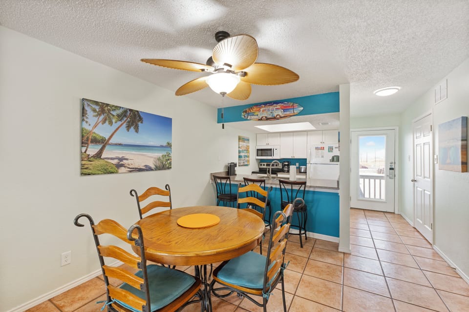 Gather around your sunny dining table where coastal vibes meet comfort. The open kitchen invites easy meal prep while beach artwork inspires vacation dreams.