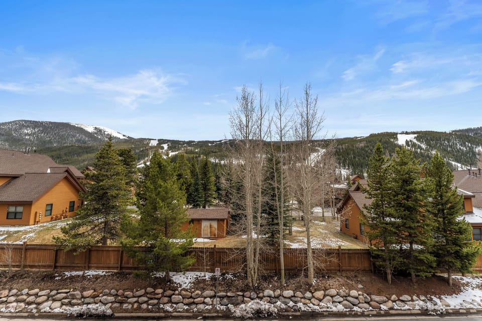 Stunning mountain community with snow-capped peaks surrounding cozy wooden homes and mature evergreen trees.