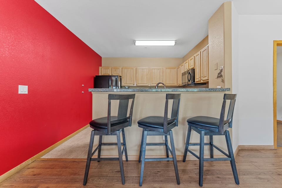 Your modern kitchen features a vibrant red accent wall and spacious granite breakfast bar where you can enjoy morning coffee or casual meals.