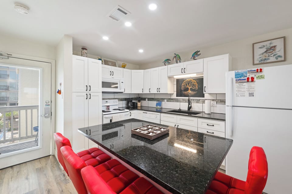 Your fully equipped kitchen features sleek granite countertops, white cabinetry, and modern appliances, perfect for preparing meals together during your stay.