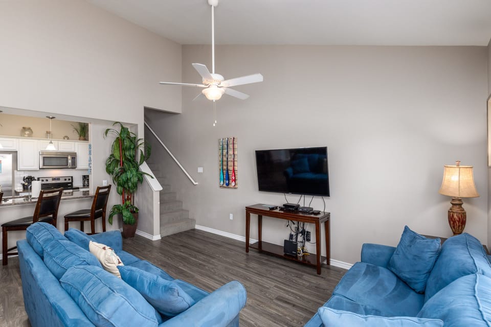 Relax in your open-concept living space with comfortable blue sofas, modern TV entertainment, and kitchen views.