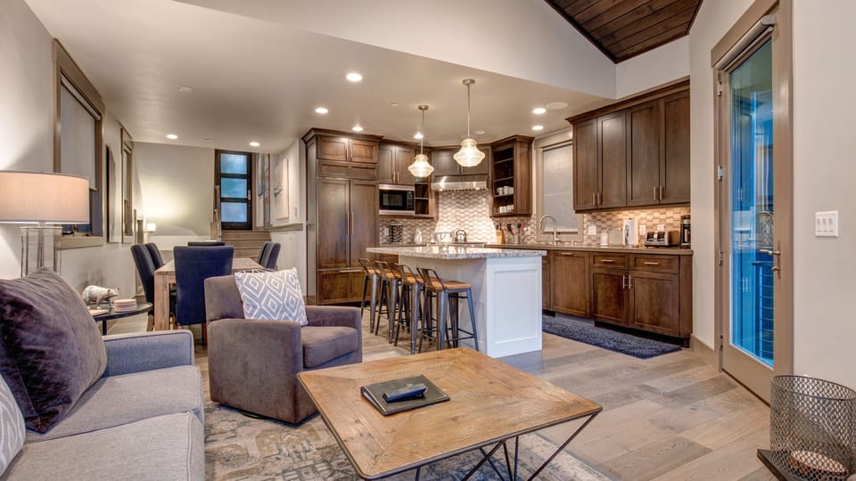 Relax in this bright, open-concept living area with a stone fireplace, vaulted wood ceiling, and kitchen bar seating. The perfect spot to unwind after a day of Park City skiing!