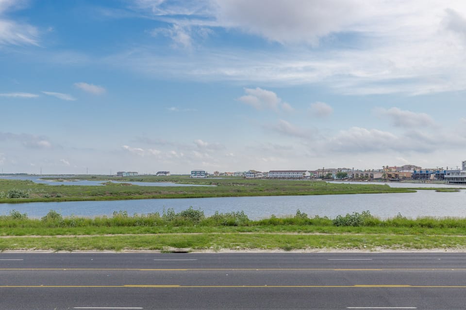 Scenic waterfront community with marshlands and residential homes stretching along the peaceful shoreline under expansive coastal skies.
