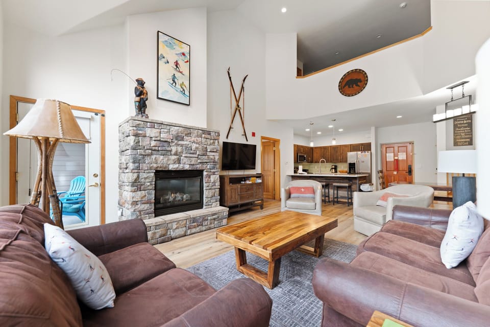 Spacious living area including vaulted ceilings, stone fireplace, floor-to-ceiling windows, and a queen sleeper sofa.