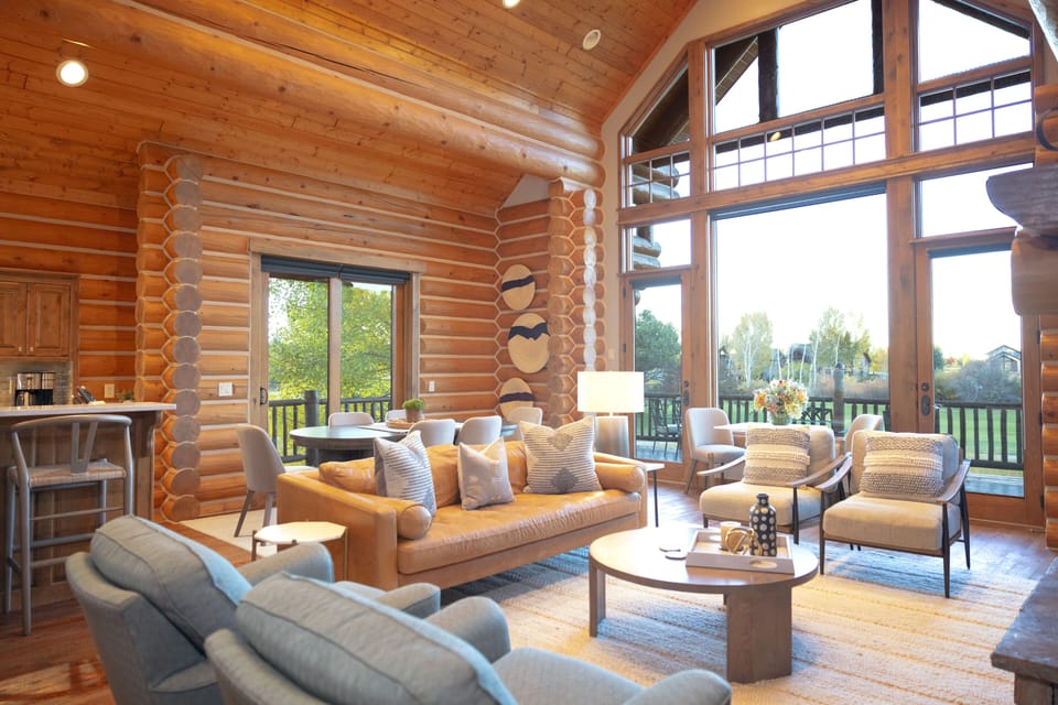 Step into your stunning log cabin retreat where soaring ceilings and floor-to-ceiling windows flood the space with natural light. Sink into plush seating by the warmth of rustic timber walls while enjoying sweeping views of the lush countryside through pan