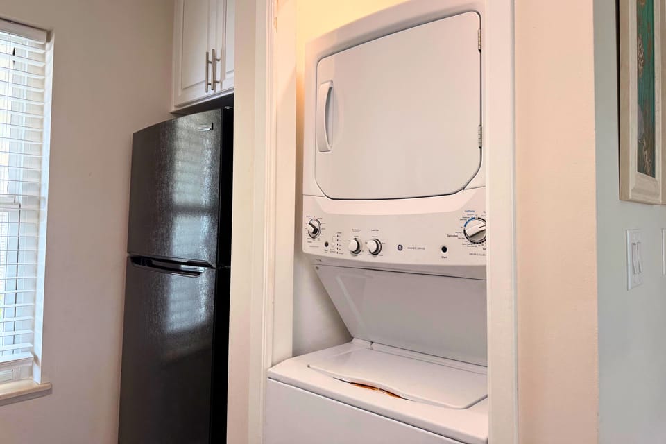 A stacked washer-dryer unit nestles conveniently in the kitchen alcove, with a sleek refrigerator nearby—so you can keep essentials close and your wardrobe fresh throughout your stay.
