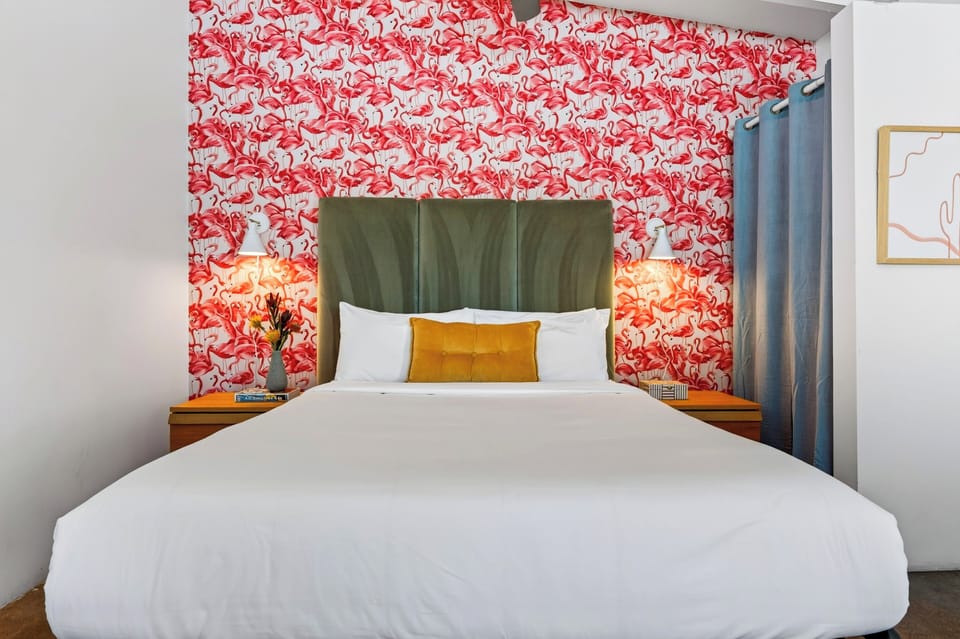 A queen bed anchors the studio, with bold flamingo wallpaper adding a playful pop of personality.