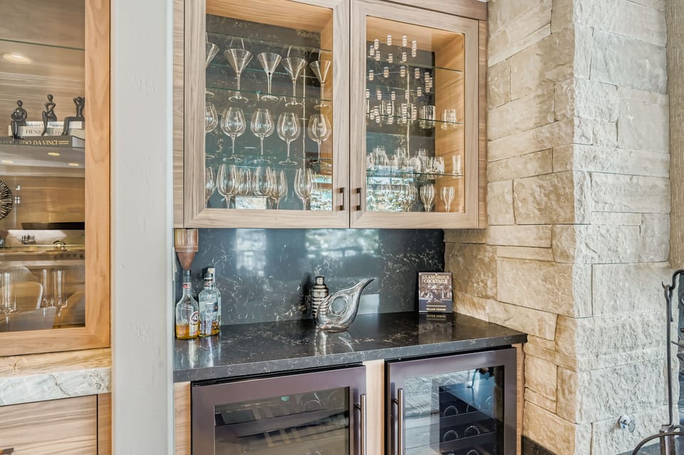 Your stylish wet bar features elegant glass cabinetry showcasing your glassware collection, perfect for entertaining with cocktails and wine.