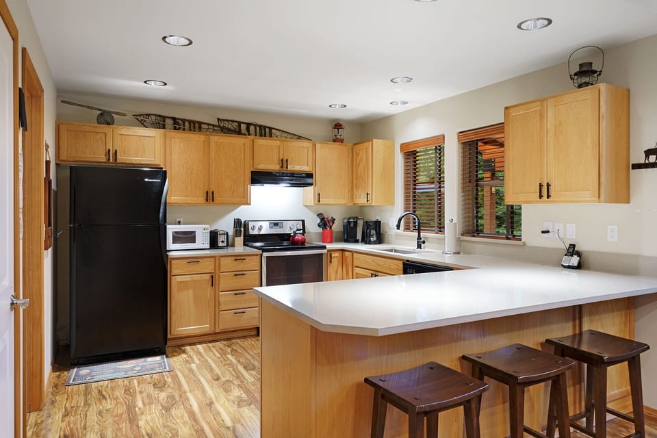Fully equipped kitchen with breakfast bar seating, warm wood cabinetry, and natural light